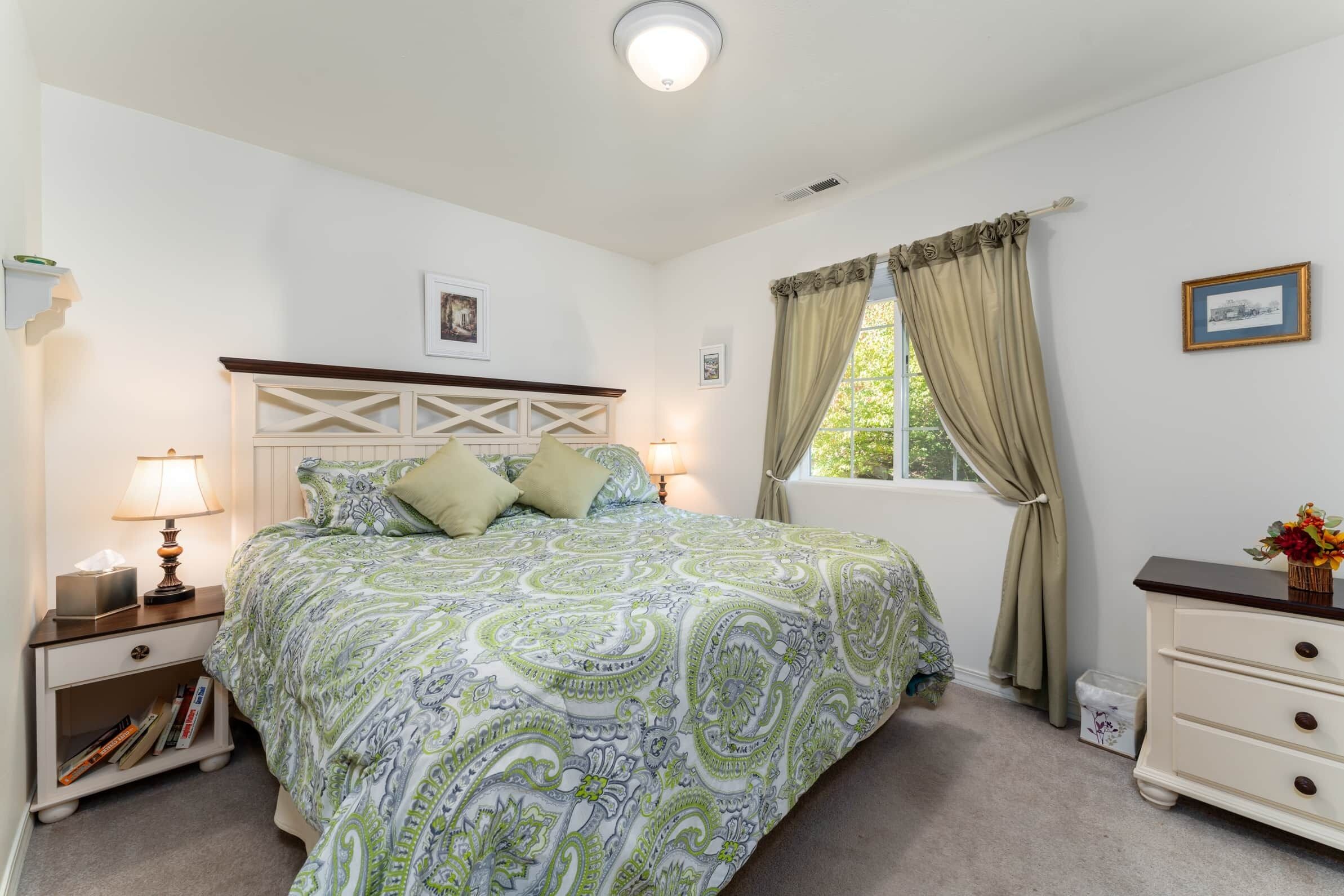 A neatly arranged bedroom with a bed, bedside tables, a dresser, and a window with curtains.