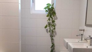 Een badkamer met witte betegelde wanden, een raam, een wastafel, een toilet en een plant.