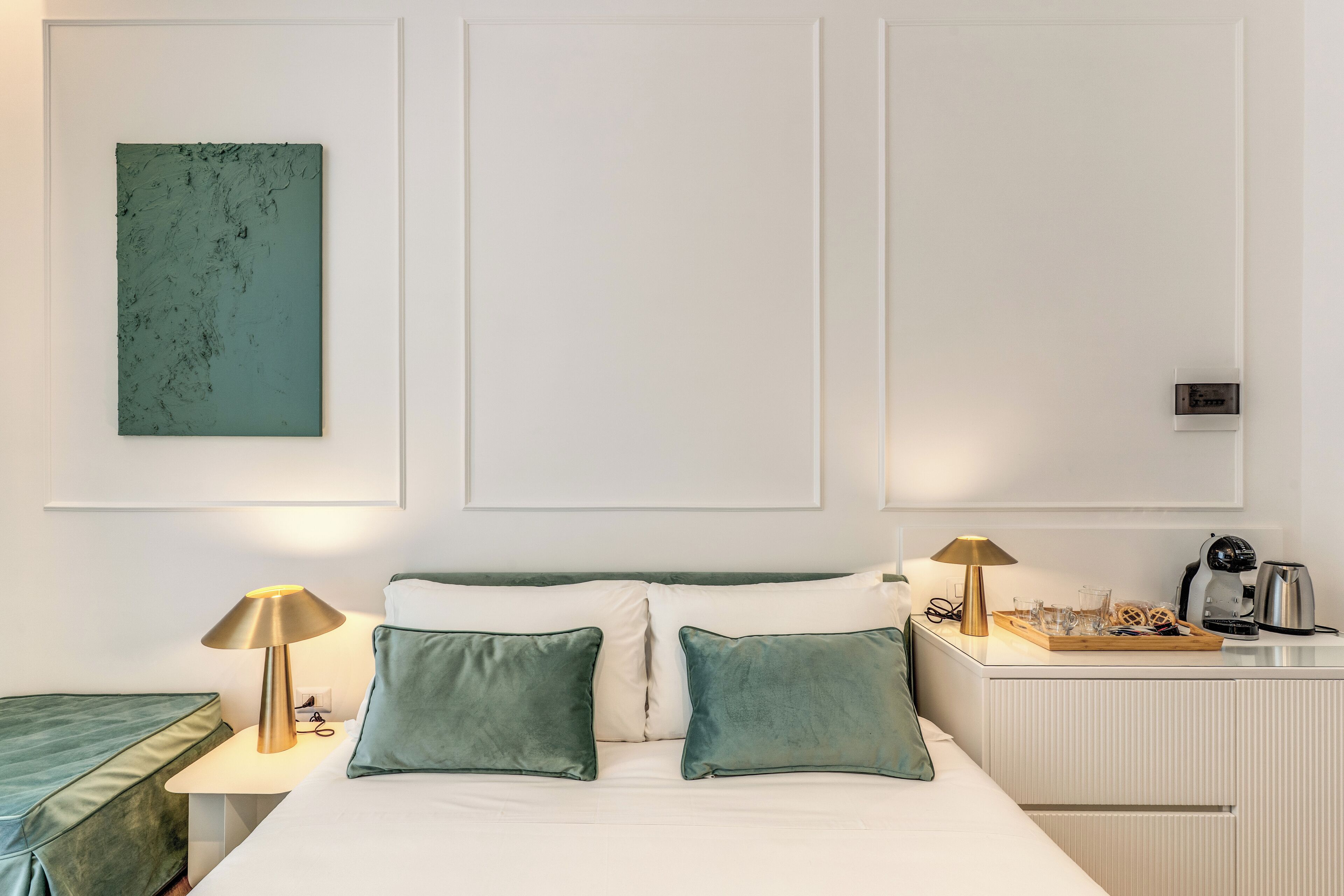 A hotel room with a bed, two bedside lamps, a coffee maker, and a tray with glasses on the nightstand.