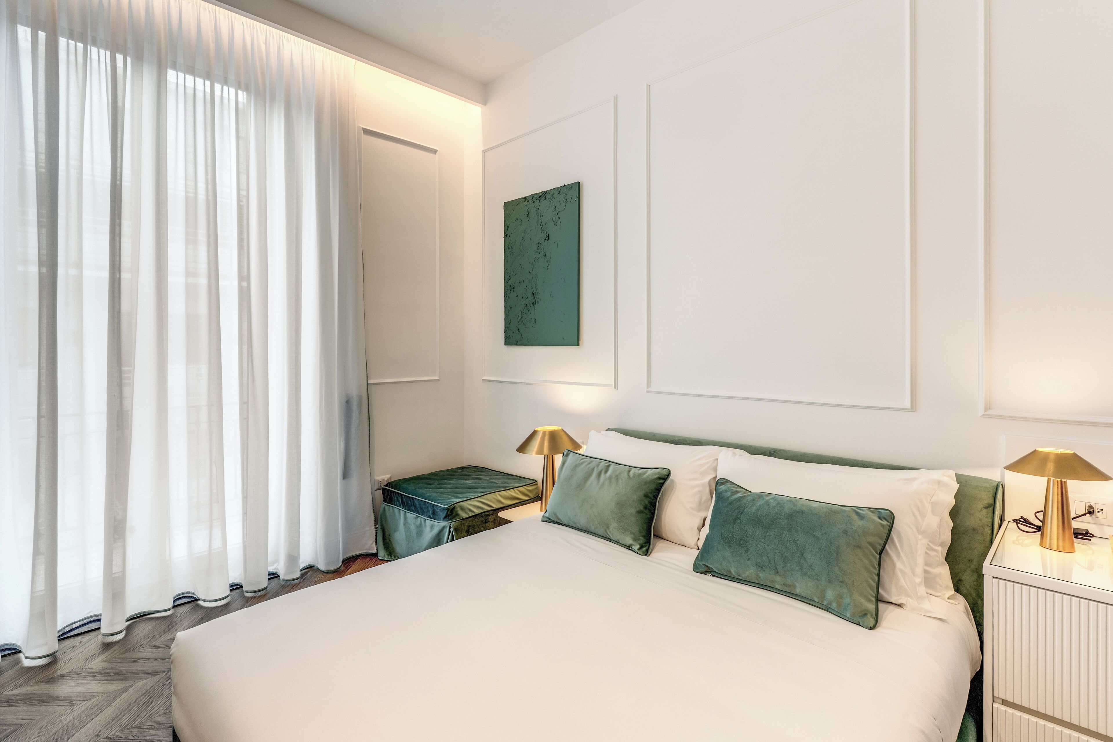 Une chambre d’hôtel avec un grand lit, deux tables de chevet avec des lampes, un coussin vert décoratif et une œuvre d’art verte accrochée au mur.