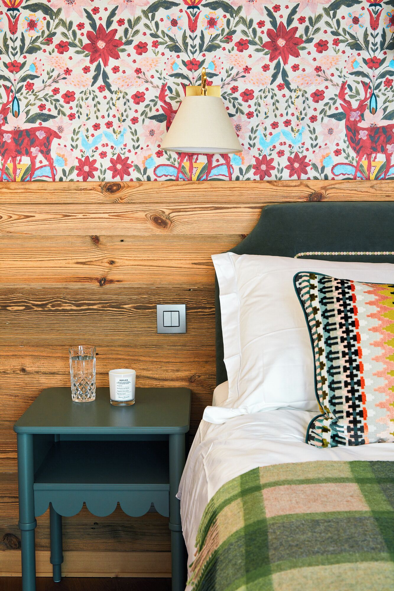 A bedroom with a wooden headboard, a nightstand with a lamp, a glass of water, and a white pillow.