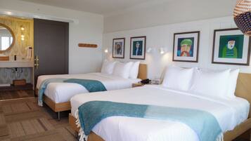 A hotel room with two beds, a bathroom with a mirror, and artwork on the walls.