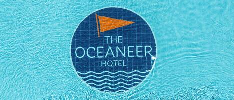 A circular logo with the text "The Oceaneer Hotel" on a blue tiled background.