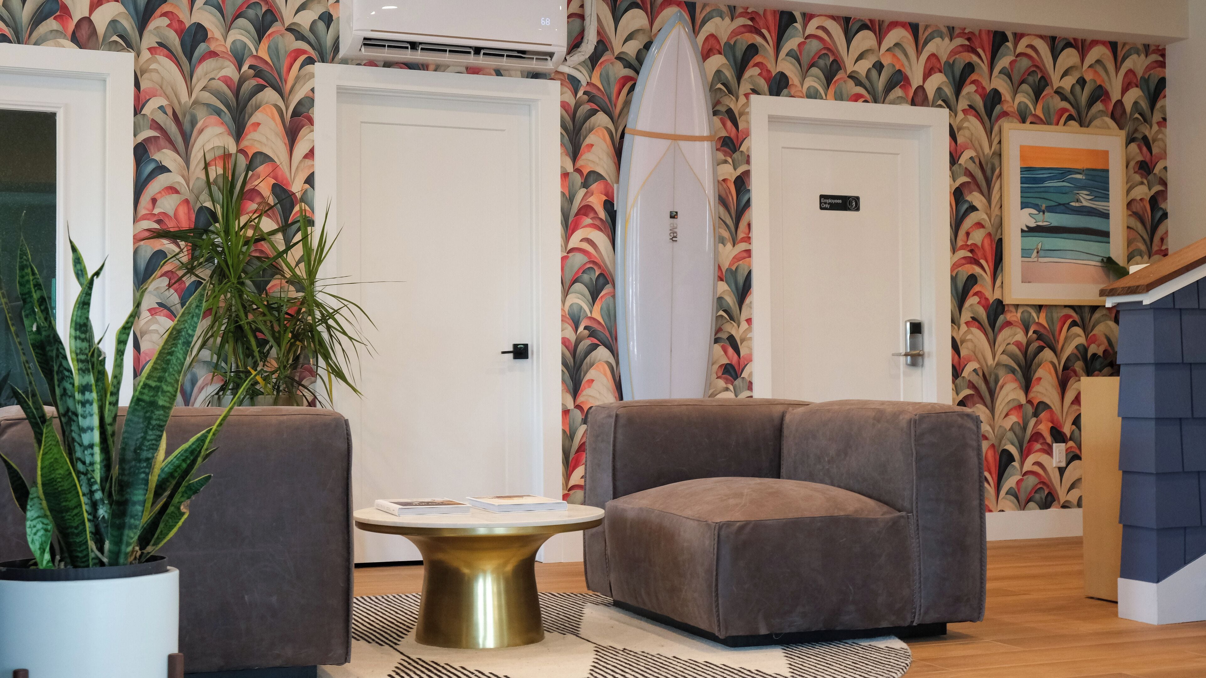 A lobby with a patterned wall, a surfboard leaning against a door, and a seating area with a coffee table.