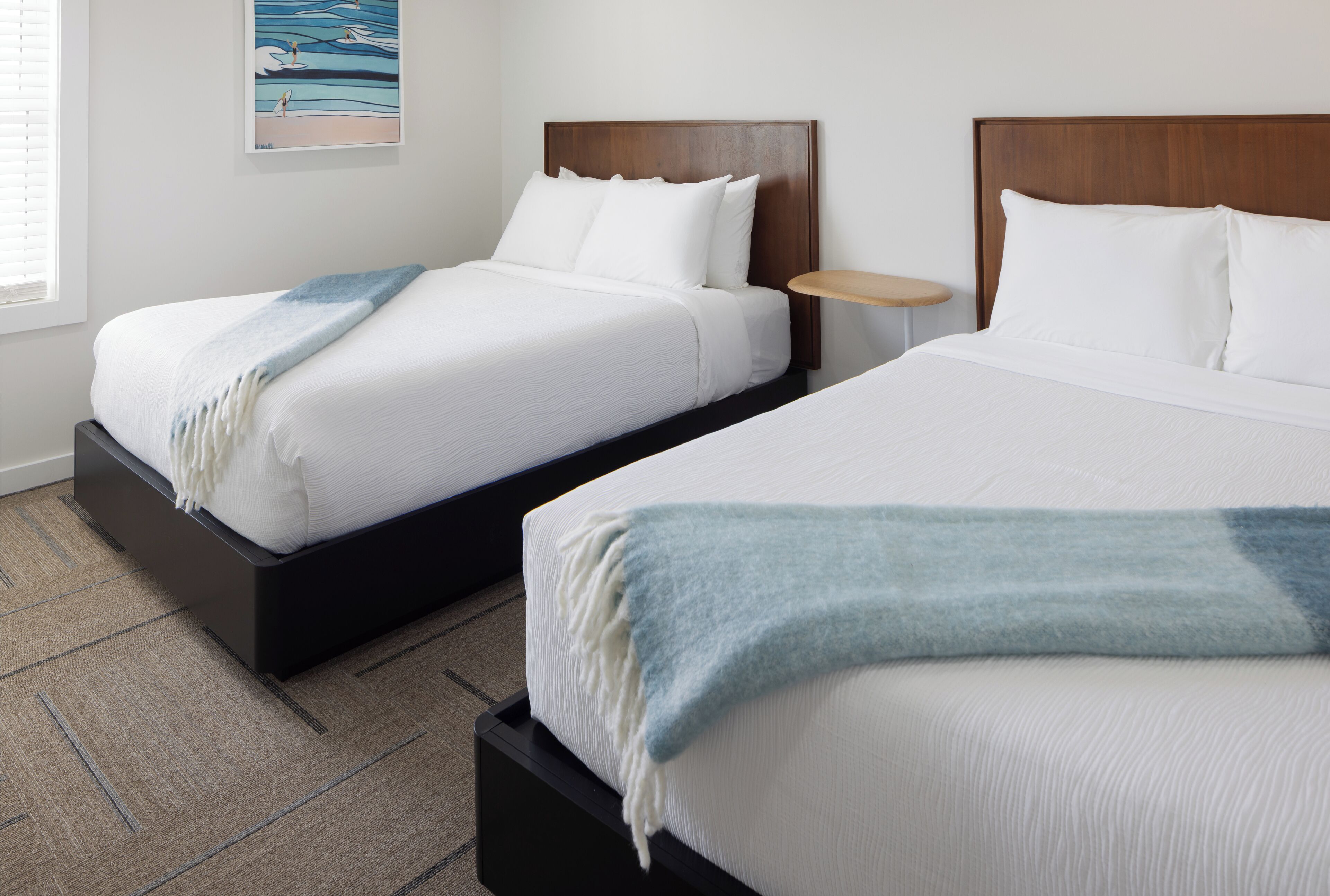 Two beds with wooden headboards, white bedding, and a blue throw blanket on one bed.