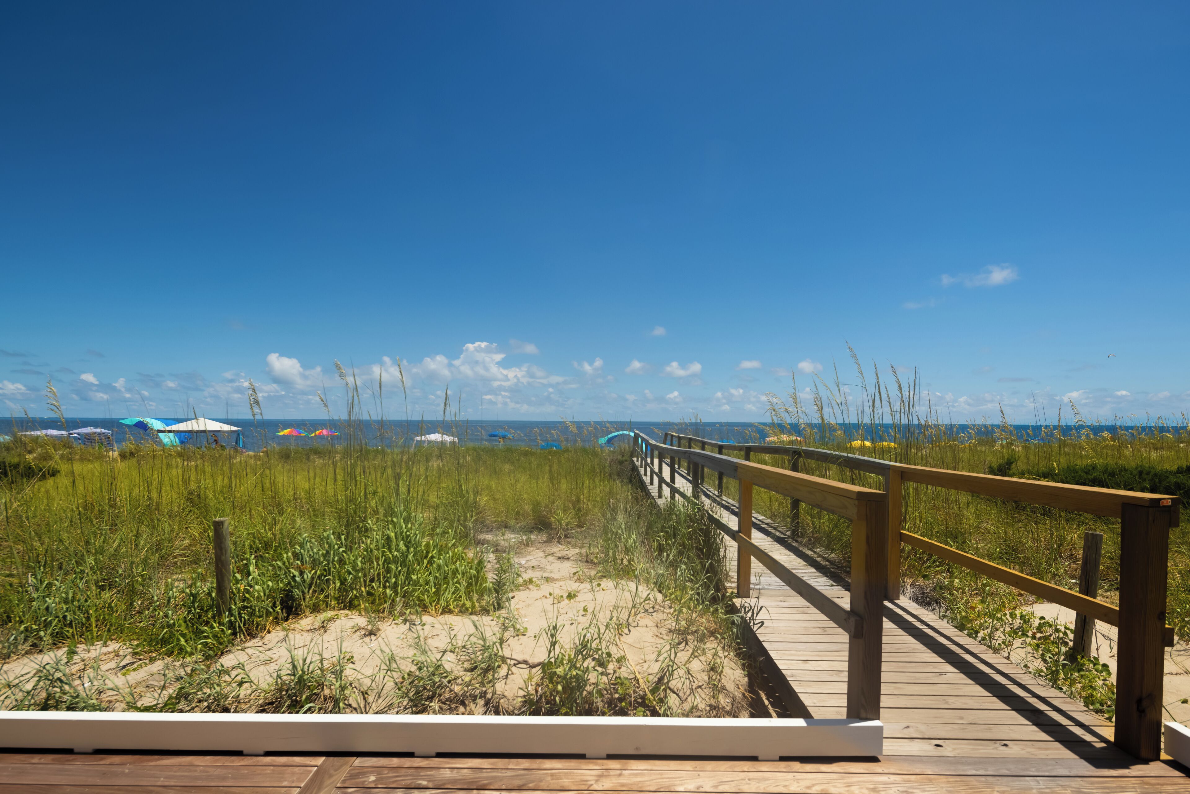 A wooden boardwalk leading to a beach with dunes and grass.