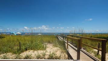 A wooden boardwalk leading to a beach with dunes and grass.