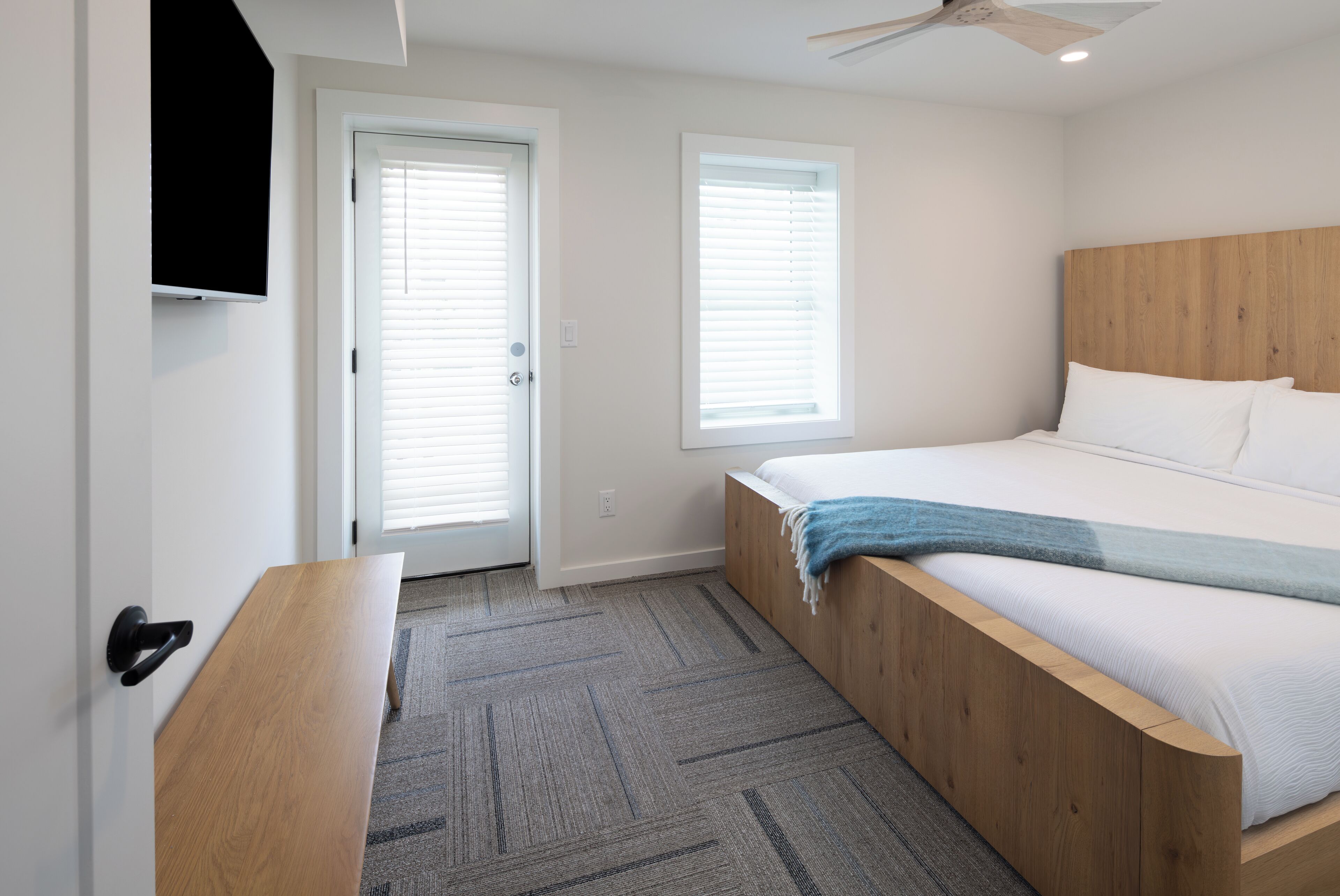 Ein Schlafzimmer mit einem Bett, einer Bank, einem Deckenventilator und zwei Fenstern mit Jalousien.