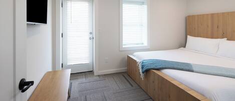 Un dormitorio con cama, un banco, ventilador de techo y dos ventanas con persianas.