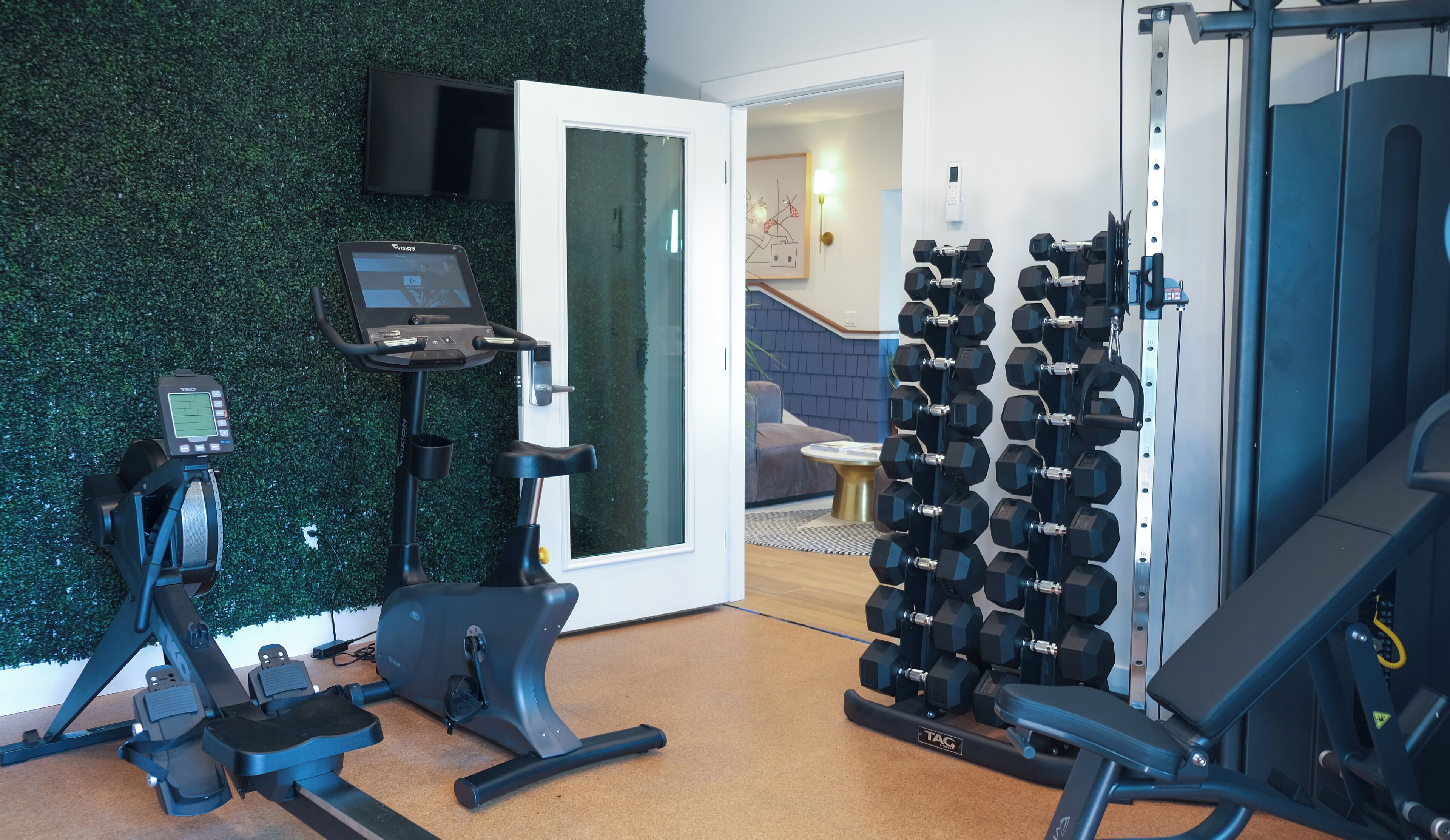 Un gimnasio en casa con una bicicleta estática, una cinta de correr y un estante con mancuernas.