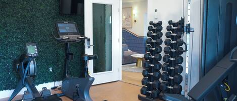 Un gimnasio en casa con una bicicleta estática, una cinta de correr y un estante con mancuernas.