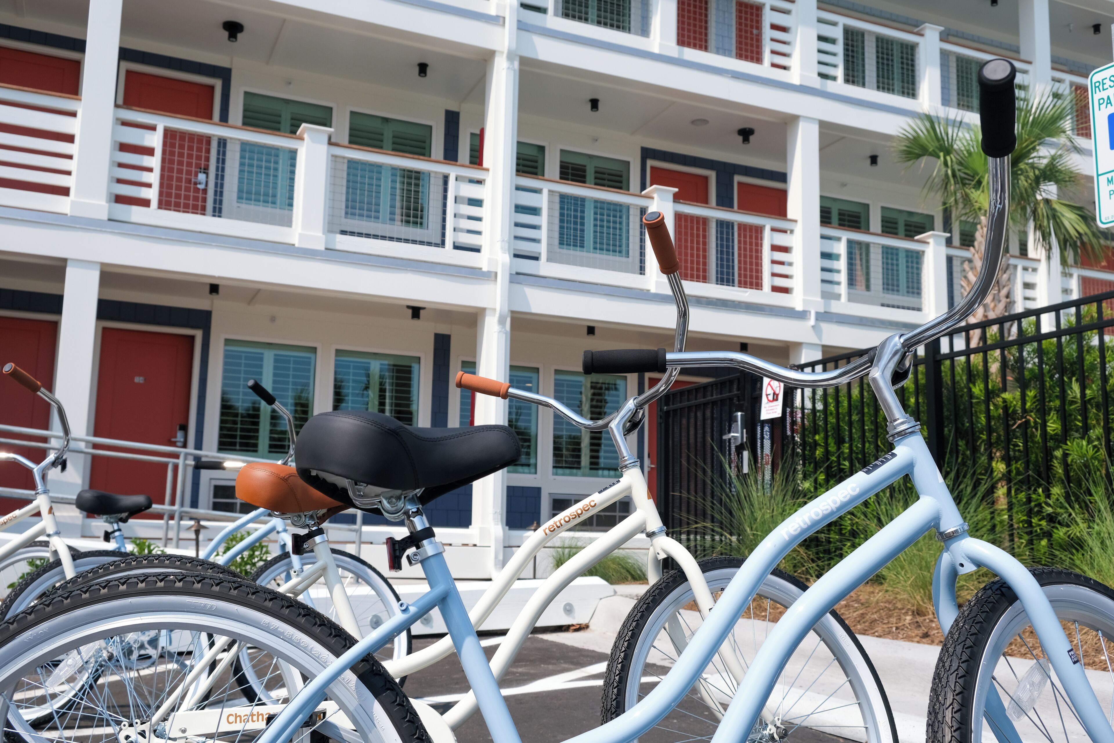 A row of bicycles parked in front of a building with balconies and red doors.