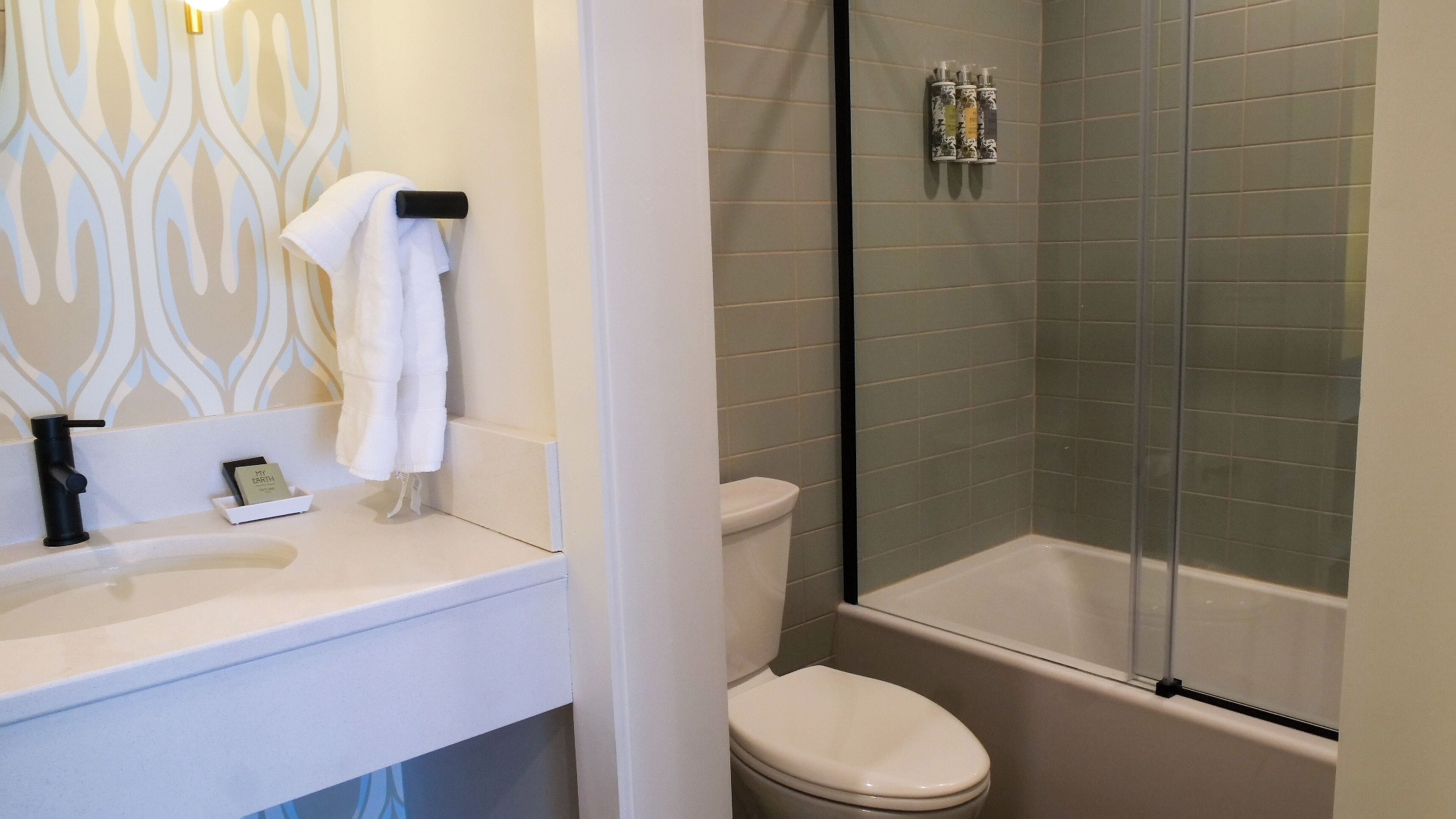 Un baño con lavamanos blanco, inodoro y ducha con mampara de vidrio.