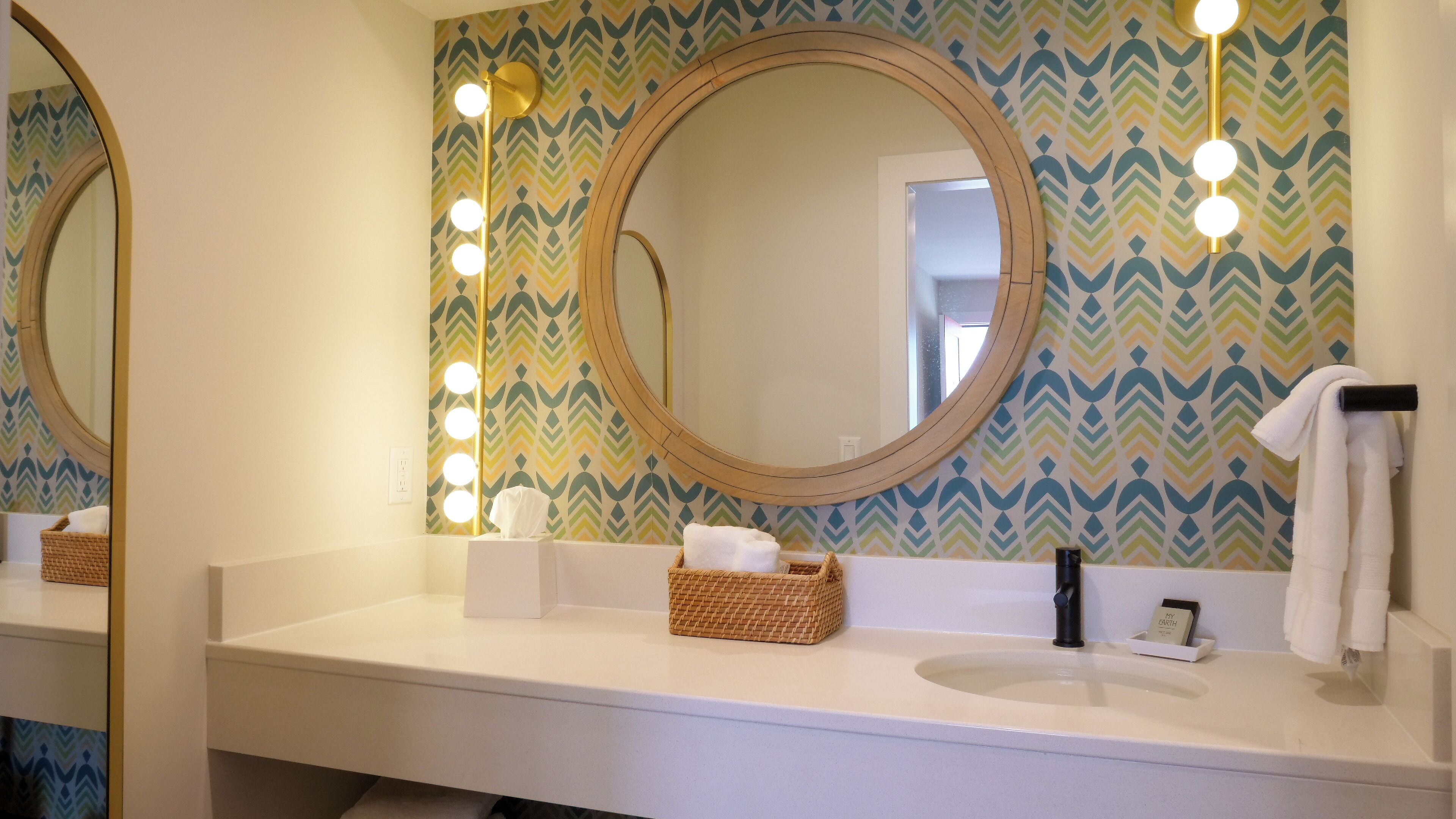Un baño con dos espejos, un tocador y un papel tapiz decorativo.
