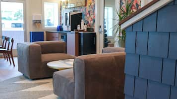 Una sala de estar moderna con dos sofás marrones, una mesita redonda y una zona de cocina con un cubo de basura y un refrigerador.