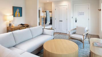 Una habitación de hotel moderna con un sofá, una mesa redonda de madera, una silla, una cama litera y una puerta con cerradura.