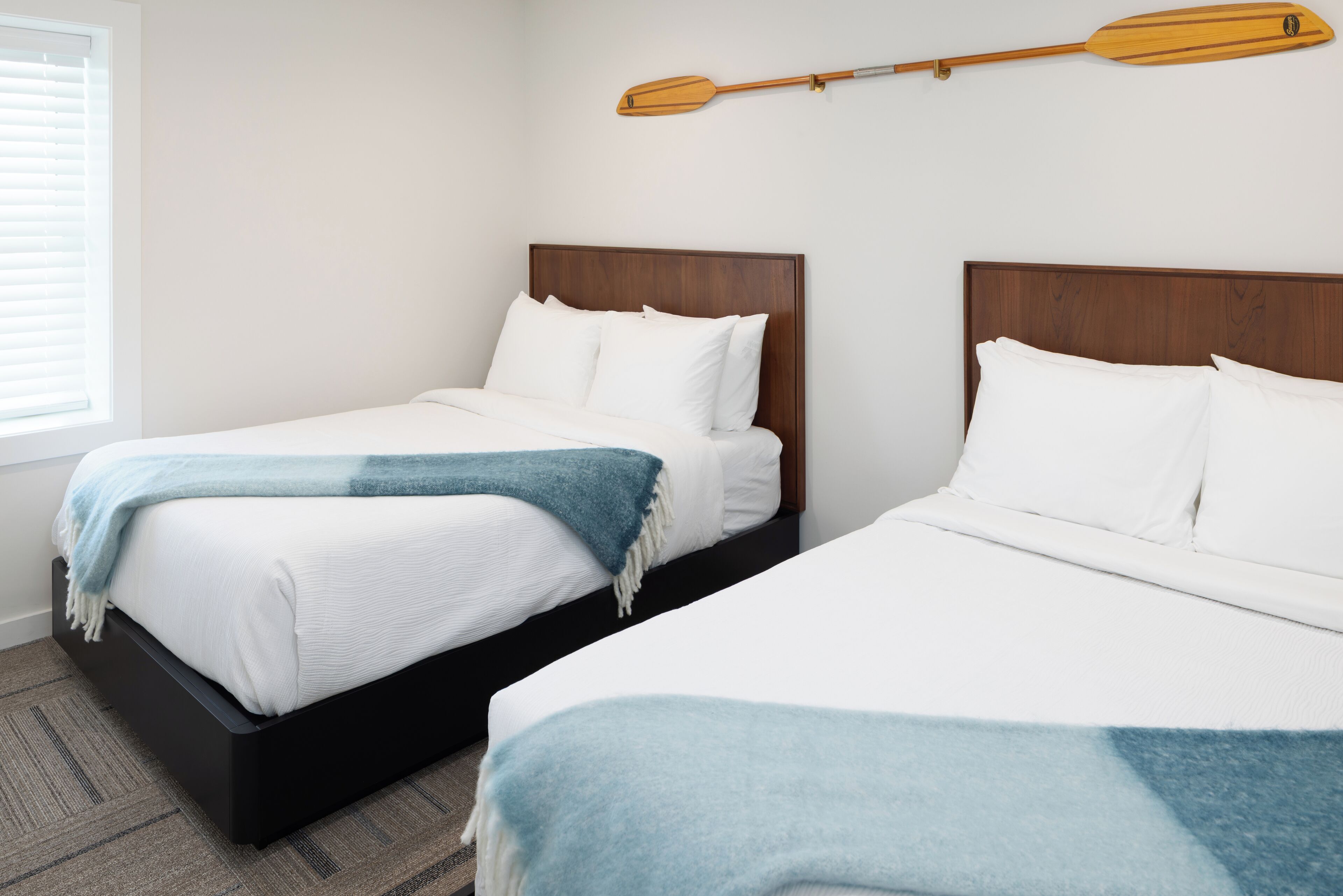 Zwei Einzelbetten mit Holz Kopfteilen, weiße Bettwäsche und eine blaue Decke.