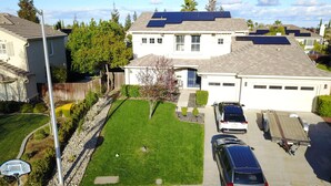 A residential house with a well-maintained lawn, solar panels on the roof, and a garage with two cars parked inside.