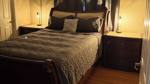 A neatly made bed with a quilted cover, two bedside tables with lamps, and a door to the left.