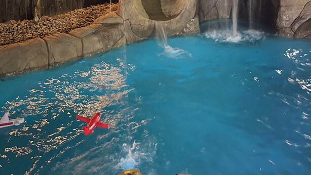 A nighttime pool area with a waterfall, wooden fence, and palm trees.