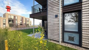 Ein modernes, zweistöckiges Gebäude mit Balkon, im Hintergrund ein roter und weißer Leuchtturm und ein QR-Code am Fenster.
