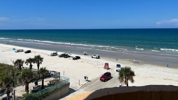 Vista de la playa con estacionamiento, palmeras y cielo despejado.