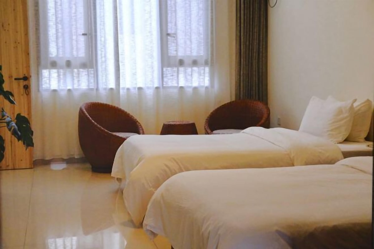 A hotel room with two beds, a wooden door, and a window with curtains.
