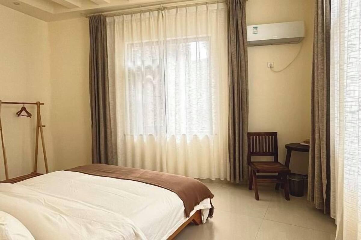 Een slaapkamer met een bed, een stoel, een klein tafeltje, een kledingrek en een airconditioning.