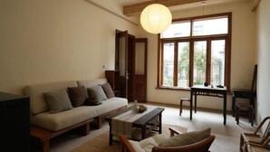 Un salon chaleureux avec un canapé, une table basse et des chaises en bois. Une grande fenêtre laisse entrer la lumière naturelle et offre une vue sur l’extérieur.