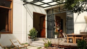 Une terrasse extérieure moderne, dotée d’une véranda en verre, de mobilier en bois et d’un petit espace jardin.