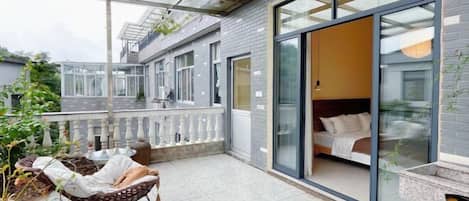 A modern bedroom with a glass door, a balcony with wicker furniture, and a view of the garden.