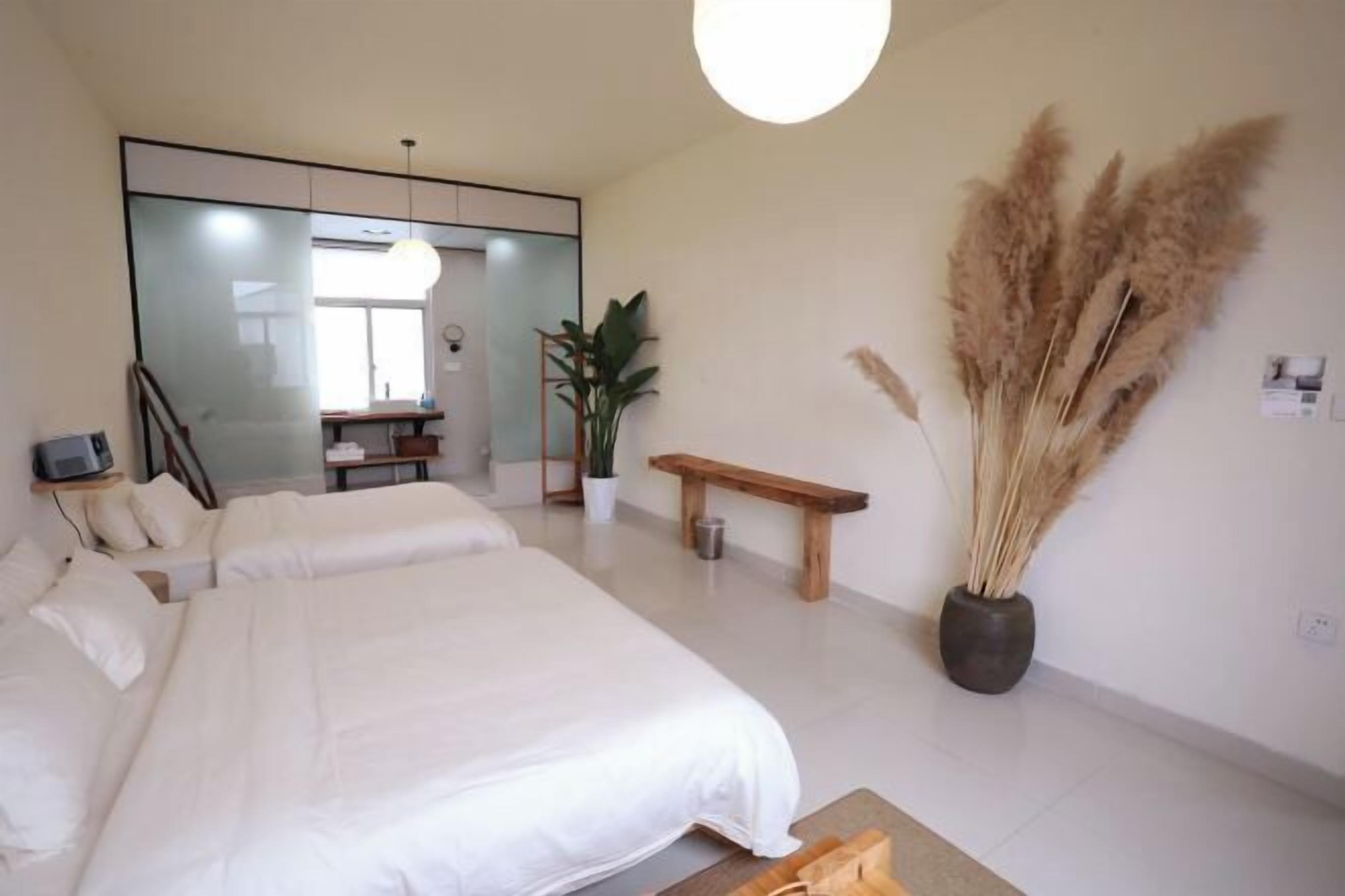 A modern bedroom with a large bed, a bedside table, a bench, a potted plant, and pampas grass.