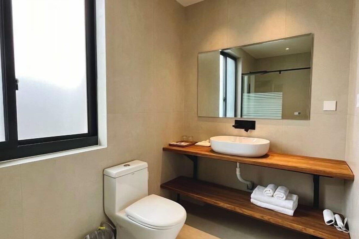 A modern bathroom with a white toilet, a wooden vanity with a white sink, a mirror above the vanity, and a towel rack with towels.