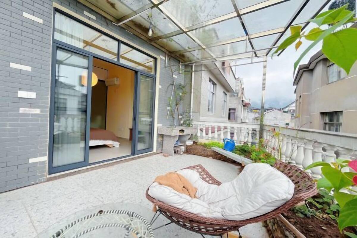 Een modern balkon met een glazen omheining, rieten meubilair en uitzicht op omliggende gebouwen.