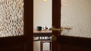 On aperçoit, à travers une porte en bois, une pièce où se trouvent une table, une chaise et une ampoule suspendue.