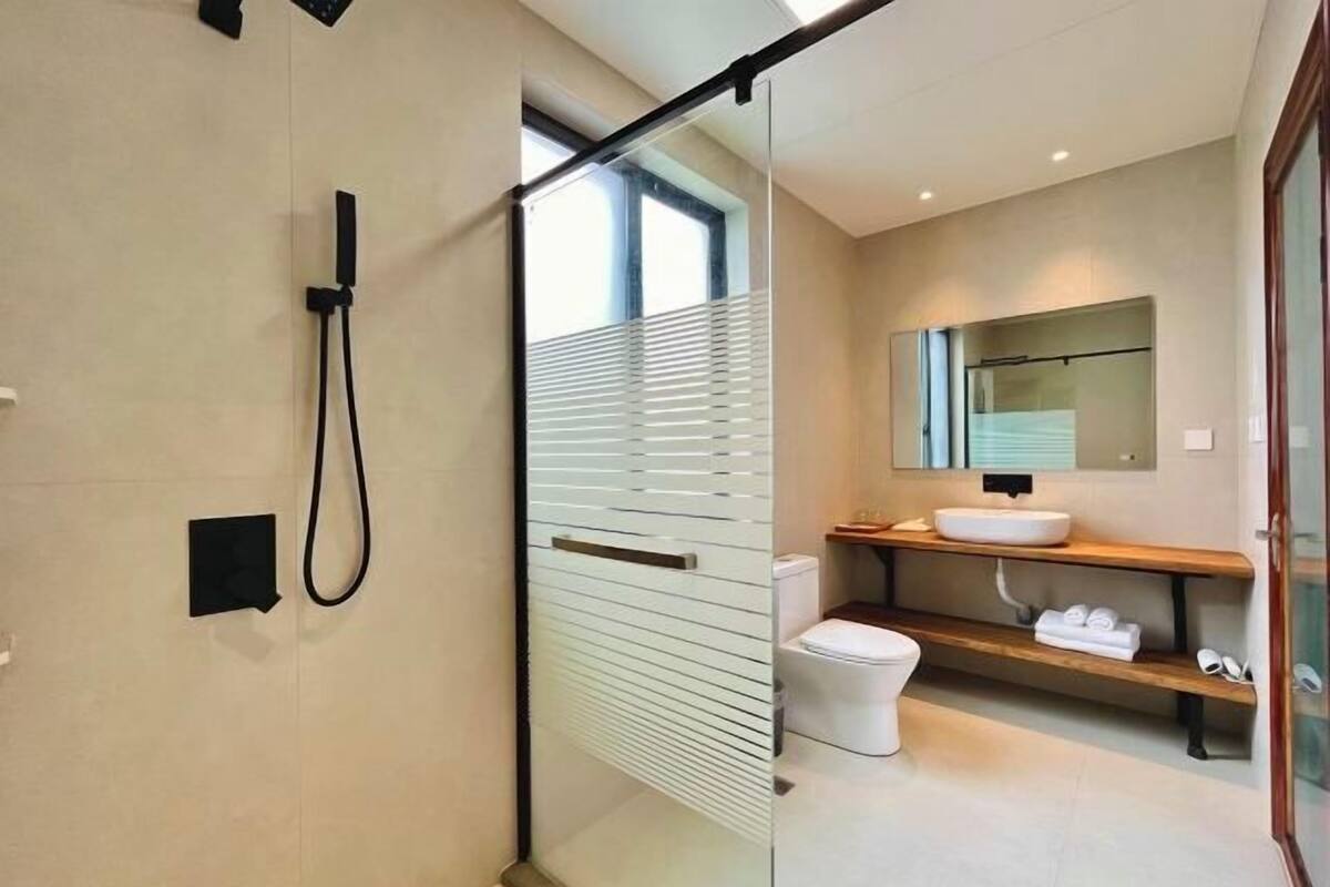 Een moderne badkamer met een douchecabine van glas, een wit wastafelmeubel en een houten plank.