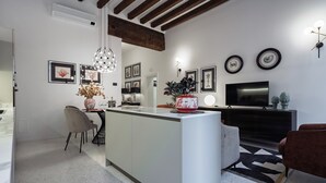 Una cocina moderna con una isla central, un área de comedor con sillas, un televisor y obras de arte enmarcadas en las paredes.