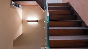Una escalera de madera con barandilla de vidrio que conduce a un nivel inferior con pared de ladrillo.