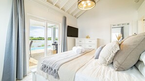 Un dormitorio con cama, televisor, cómoda y vistas a una piscina y vegetación.