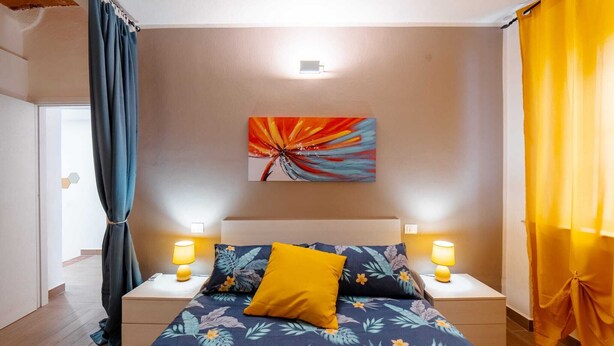 A bedroom with a bed, two bedside lamps, a nightstand, a wall-mounted artwork, and curtains. - R&R House 5' walk from the Tower! Private interior courtyard !!! (Pisa)