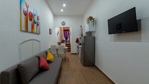 A compact living space with a sofa, a dining table, a kitchen area, and a TV mounted on the wall. - R&R House 5' walk from the Tower! Private interior courtyard !!! (Pisa)