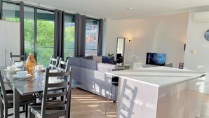 A modern living room with a dining area, large windows, a sofa, a TV, and a kitchen island. - Sleek 3-bedroom flat with life in Southward, Bourough near The Shard (London)