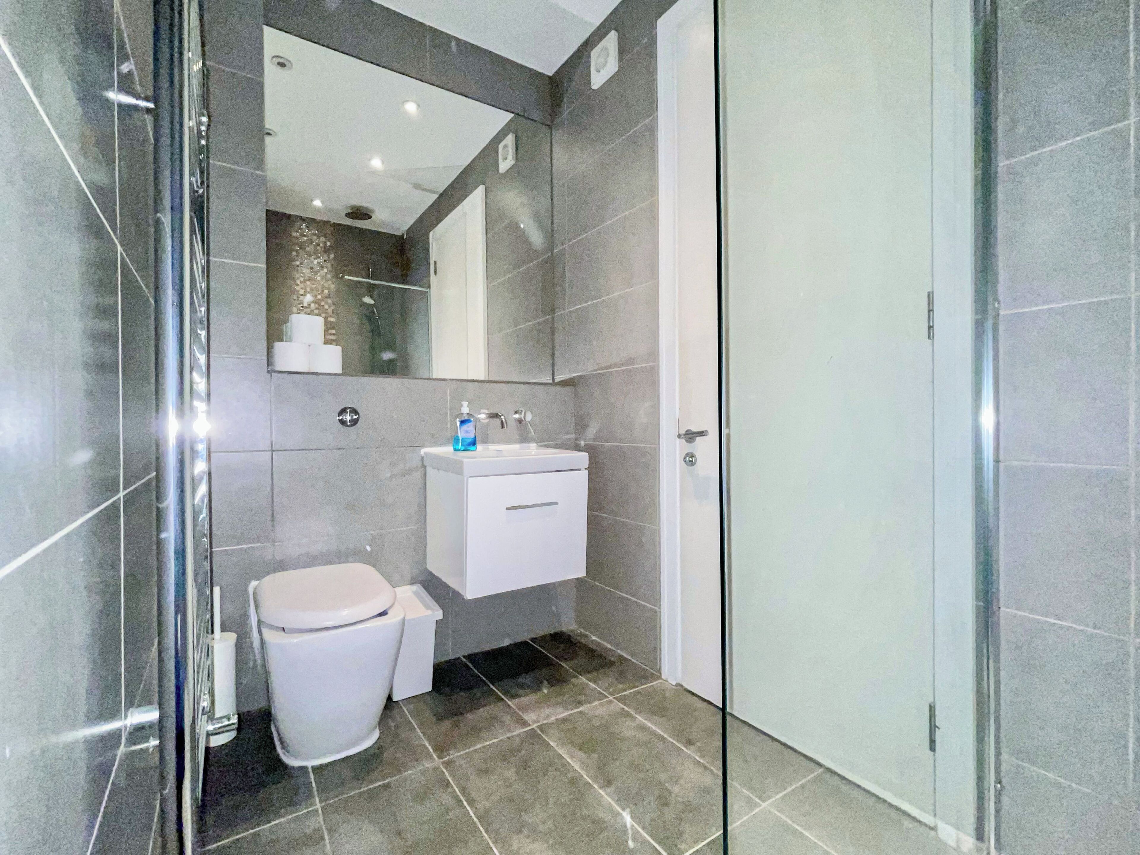 Un baño moderno con cabina de ducha de vidrio, un lavamanos blanco y un inodoro.
