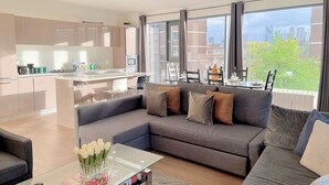 A modern living room with a grey sofa, a glass coffee table, and a view of the city through large windows. - Sleek 3-bedroom flat with life in Southward, Bourough near The Shard (London)