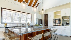 Een moderne keuken met een groot eiland, barstoelen en witte kastjes.
