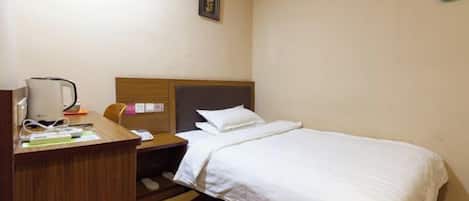 A hotel room with a bed, a desk with a lamp, and a wall-mounted picture.