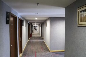 Un couloir d’hôtel avec des portes, un sol recouvert de moquette et un tableau encadré accroché au mur.