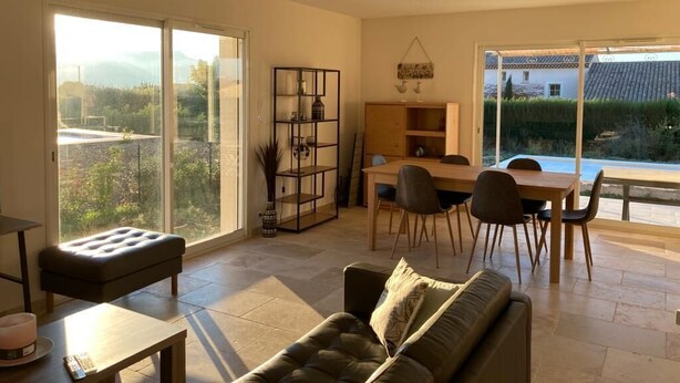A modern living room with a sofa, a dining table with chairs, and a large window offering a view of greenery and a building. - Rasteau, vacation villa with 3 bedrooms and heated pool (Rasteau)