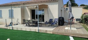 A house with a patio area featuring a table and chairs, a covered seating area, and a wooden deck.