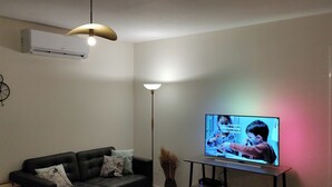 A living room with a black leather sofa, a television on a stand, a floor lamp, and a wall-mounted air conditioner. - Rasteau, vacation villa with 3 bedrooms and heated pool (Rasteau)
